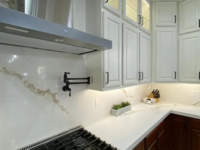 Range hood and pot filler against a marbled quartz backsplash