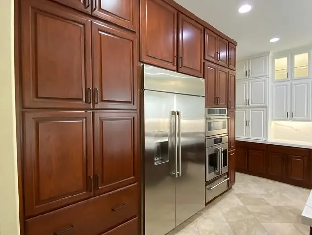 Tall cherry pantry cabinets beside a stainless refrigerator and double ovens
