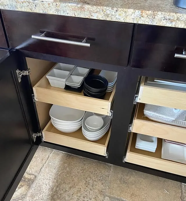Roll-out shelves holding plates and bowls inside dark base cabinets