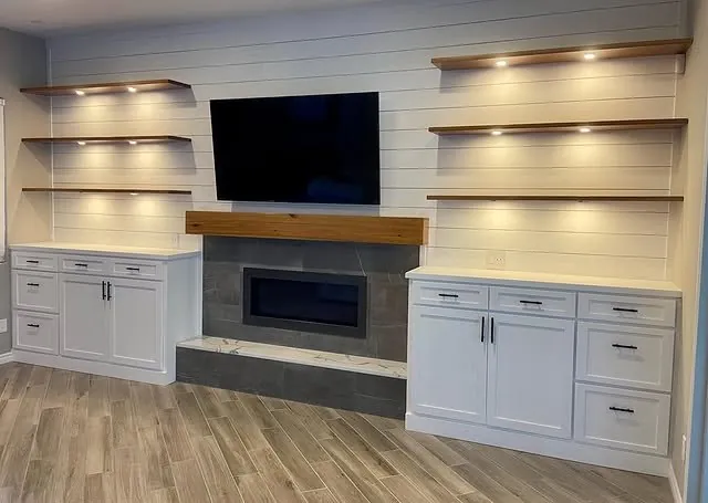 Wide view of the shiplap wall with floating shelves and white cabinets either side of the fireplace