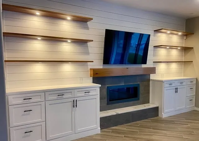Floating shelves lit by puck lights above white base cabinets