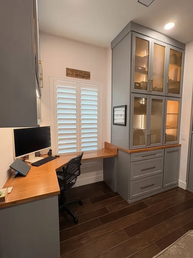 Grey office cabinetry to the ceiling with glass-front uppers and a cherry desk