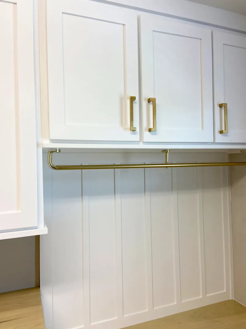 A brass hanging rod under white wall cabinets