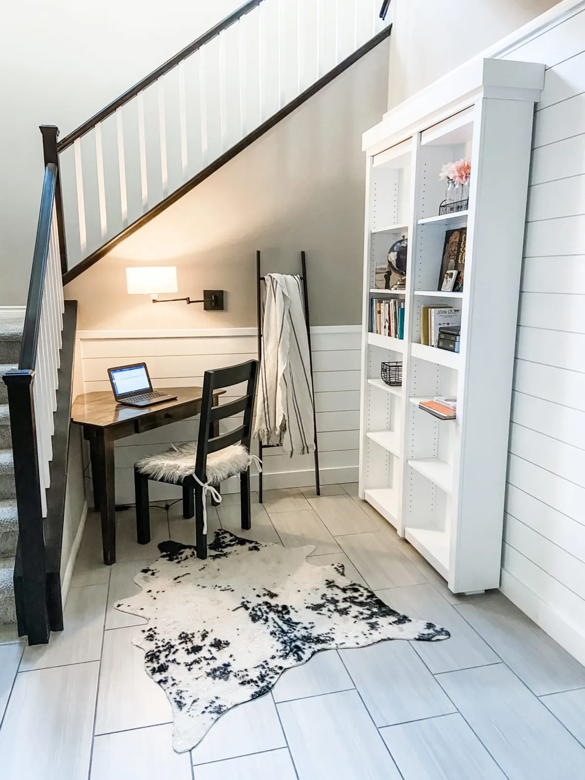 Desk and bookcase built under a staircase, with shiplap and a wall lamp